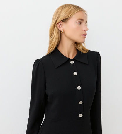 A woman with blonde hair models the Lucia Black Midi Shirt Dress, featuring pearl-look buttons and a pointed collar—ideal for office-to-evening style. She looks to the side against a plain white background.