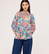 A woman wearing the Lizzie Green Floral Jersey Blouse with long sleeves stands against a plain, light background, pairing it with loose blue jeans.