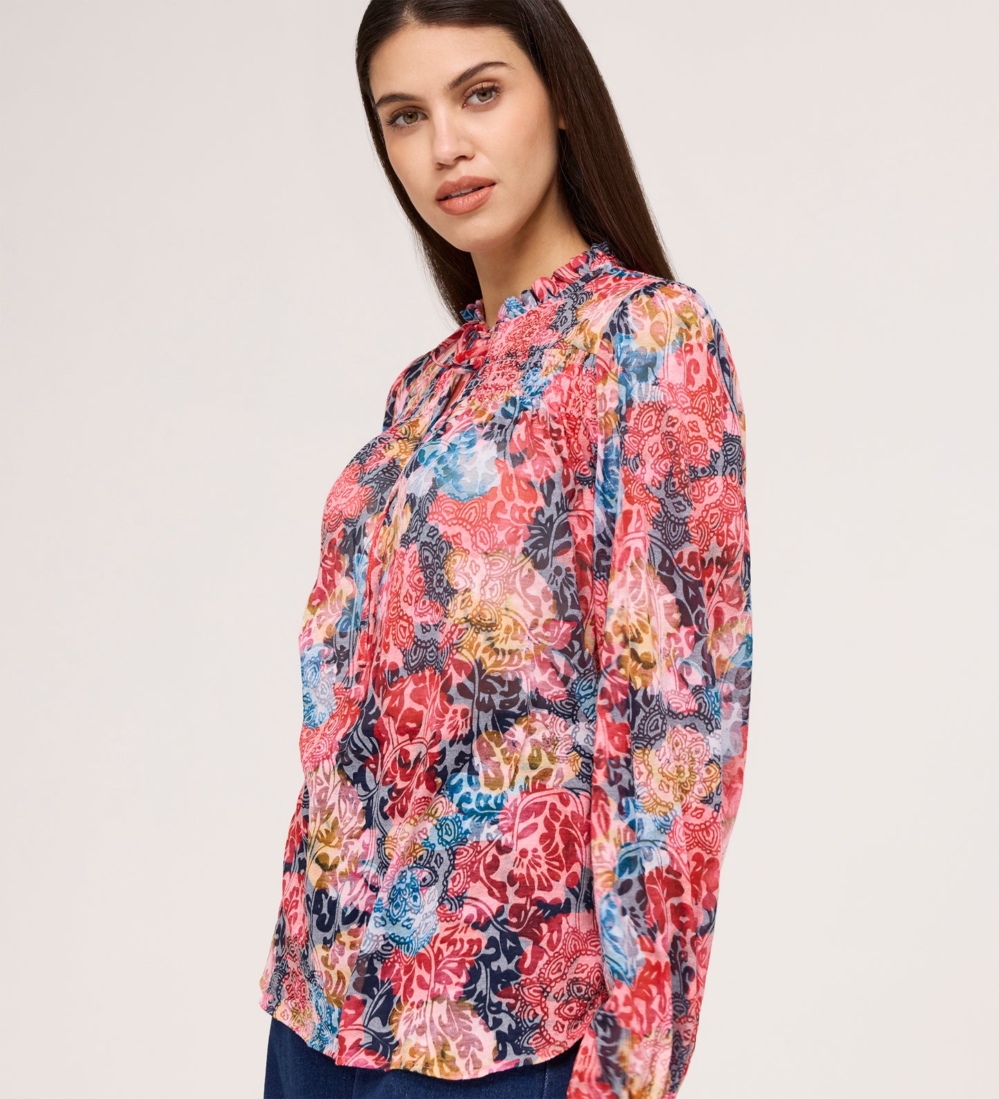 A woman with long dark hair wears the Lizzie Pink Floral Jersey Blouse, standing against a plain light background and looking slightly to the side with a subtle smile.