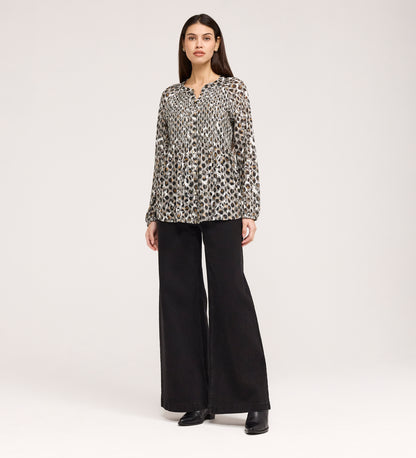 A woman stands facing forward against a plain light background, wearing the Martha Khaki Animal Jersey Blouse with black and beige spots, textured shirring, wide-leg black pants, and black shoes.