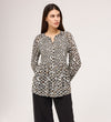 A woman with long brown hair looks to the side, wearing the Martha Khaki Animal Jersey Blouse—a long-sleeve, button-up top with a black, brown, and white animal print—paired with loose black pants against a plain background.