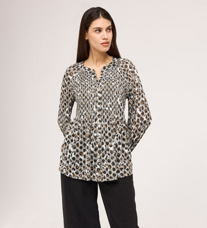 A woman with long brown hair looks to the side, wearing the Martha Khaki Animal Jersey Blouse—a long-sleeve, button-up top with a black, brown, and white animal print—paired with loose black pants against a plain background.