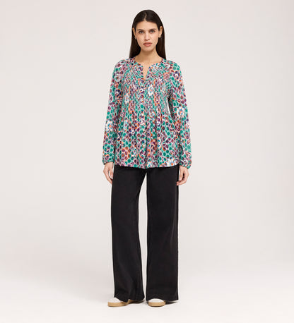 A woman stands facing forward in the Martha Green Floral Jersey Blouse with textured shirring, loose black flare-hem pants, and beige shoes, set against a plain light background.