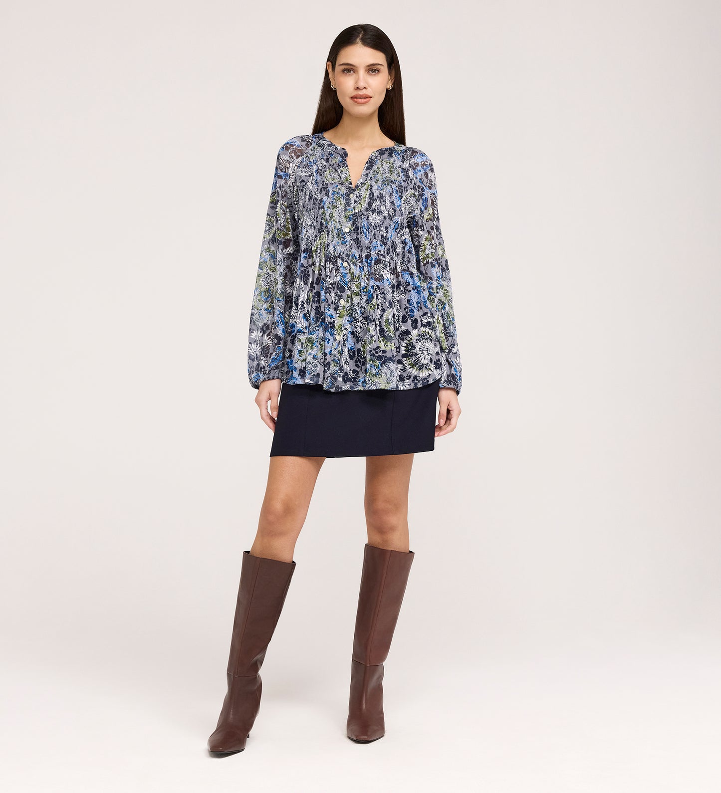A woman stands facing forward, wearing a loose Martha Navy Floral Jersey Blouse with textured shirring, a dark navy mini skirt with a slight flare hem, and knee-high brown boots against a plain light background.