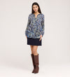 A woman stands against a plain background wearing the Martha Navy Floral Jersey Blouse, a dark mini skirt, and knee-high brown boots. She faces forward with her hands relaxed by her sides.