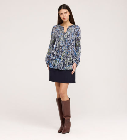 A woman stands against a plain background wearing the Martha Navy Floral Jersey Blouse, a dark mini skirt, and knee-high brown boots. She faces forward with her hands relaxed by her sides.