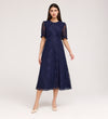 A woman poses against a light background in the Mela Navy Lace Midi Dress, featuring an elegant round neckline, short puff sleeves, and paired with beige heels.