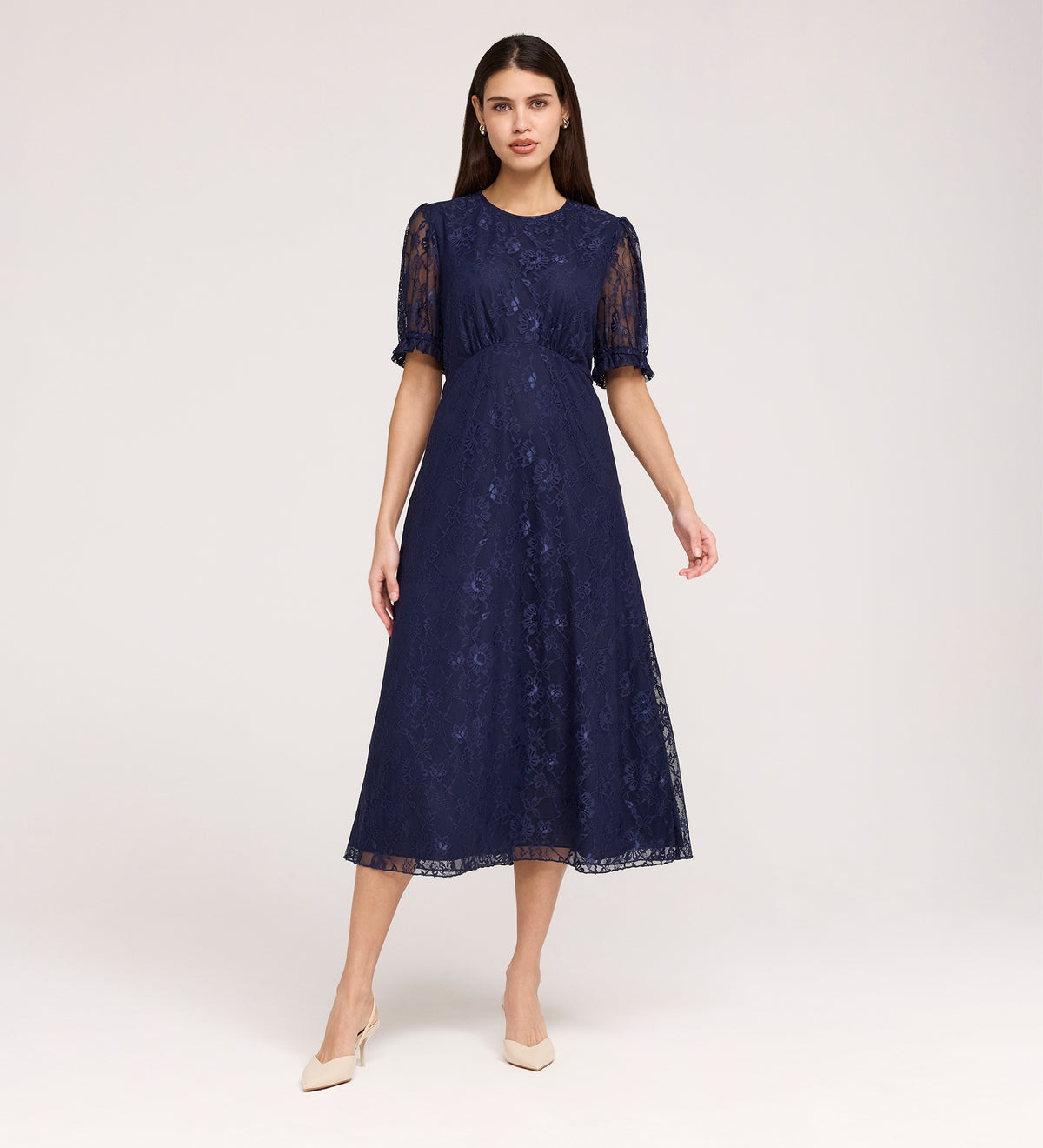 A woman poses against a light background in the Mela Navy Lace Midi Dress, featuring an elegant round neckline, short puff sleeves, and paired with beige heels.