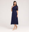 A woman poses in the Mela Navy Lace Midi Dress, featuring a knee-length lace design with a round neckline and short sleeves, paired with beige pointed heels against a plain light background.