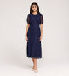 A woman with straight dark hair and a neutral expression models the Mela Navy Lace Midi Dress, featuring an elegant round neckline and short puffed sleeves, paired with beige pointed-toe shoes against a plain backdrop.