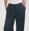 Someone wears the Nat Navy Polka Dot Wide Leg Trousers with an elasticated waist, styled with a white fitted top and hands in the pockets.