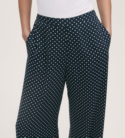 Someone wears the Nat Navy Polka Dot Wide Leg Trousers with an elasticated waist, styled with a white fitted top and hands in the pockets.