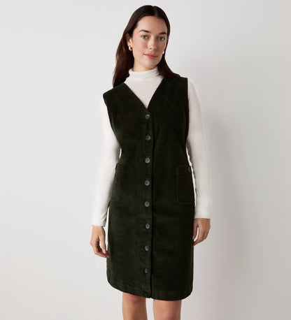 A woman with long dark hair stands against a plain white background wearing the Reneka Khaki Corduroy Knee Length Dress over a white turtleneck, looking at the camera with a slight smile.