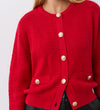 A woman wears the Saskia Red Button Up Cotton Cardigan with gold crest buttons and two front pockets, styled with black pants. The image is cropped at the neck and waist.