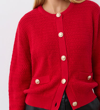 A woman wears the Saskia Red Button Up Cotton Cardigan with gold crest buttons and two front pockets, styled with black pants. The image is cropped at the neck and waist.
