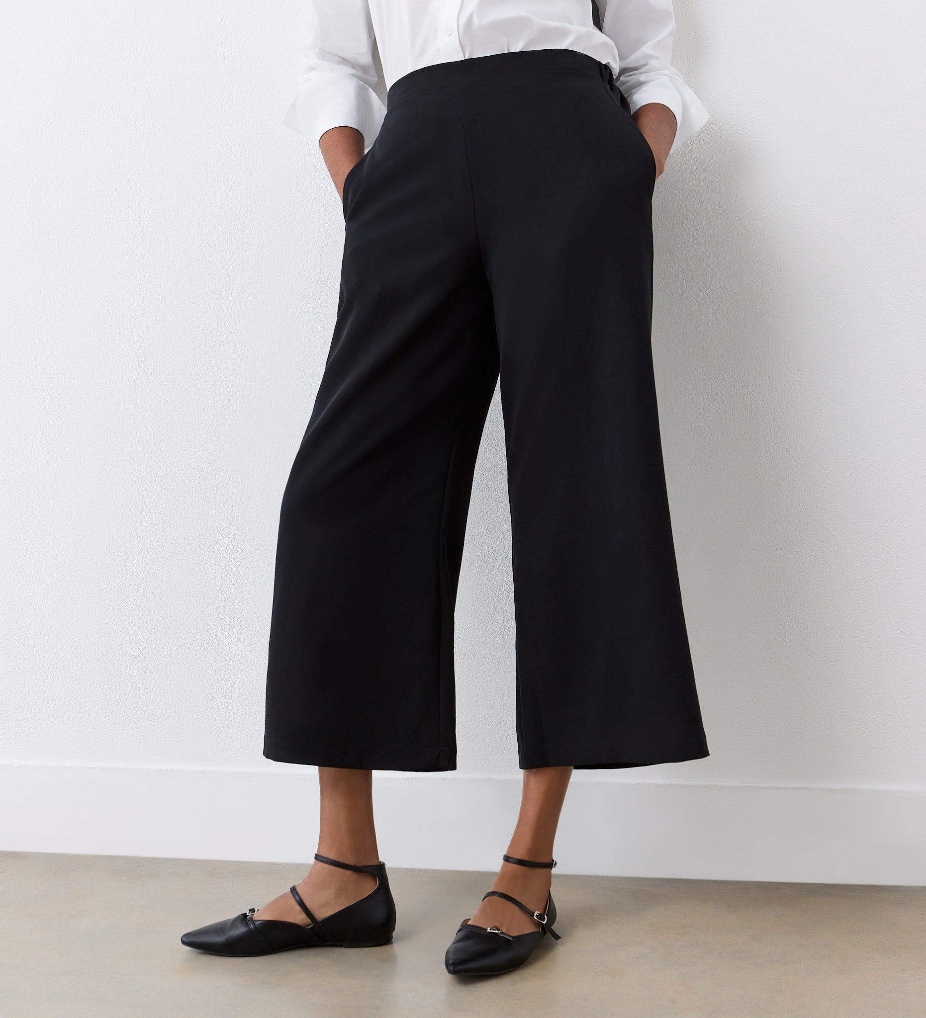 Wearing Simone Black Cropped Wide Leg Trousers with an elasticated waistband, a white long-sleeve shirt, and black pointed-toe flats, this look is perfect for a stylish wardrobe.