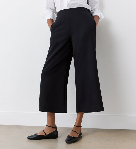 Wearing Simone Black Cropped Wide Leg Trousers with an elasticated waistband, a white long-sleeve shirt, and black pointed-toe flats, this look is perfect for a stylish wardrobe.