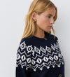 A woman with blonde hair and gold hoop earrings wears the Violet Navy Cotton Cardigan, featuring a round neckline and brown buttons, standing against a plain white wall.
