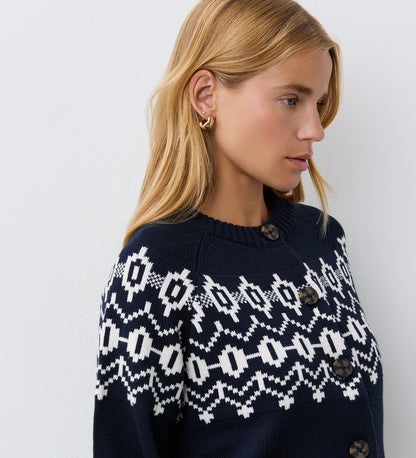 A woman with blonde hair and gold hoop earrings wears the Violet Navy Cotton Cardigan, featuring a round neckline and brown buttons, standing against a plain white wall.