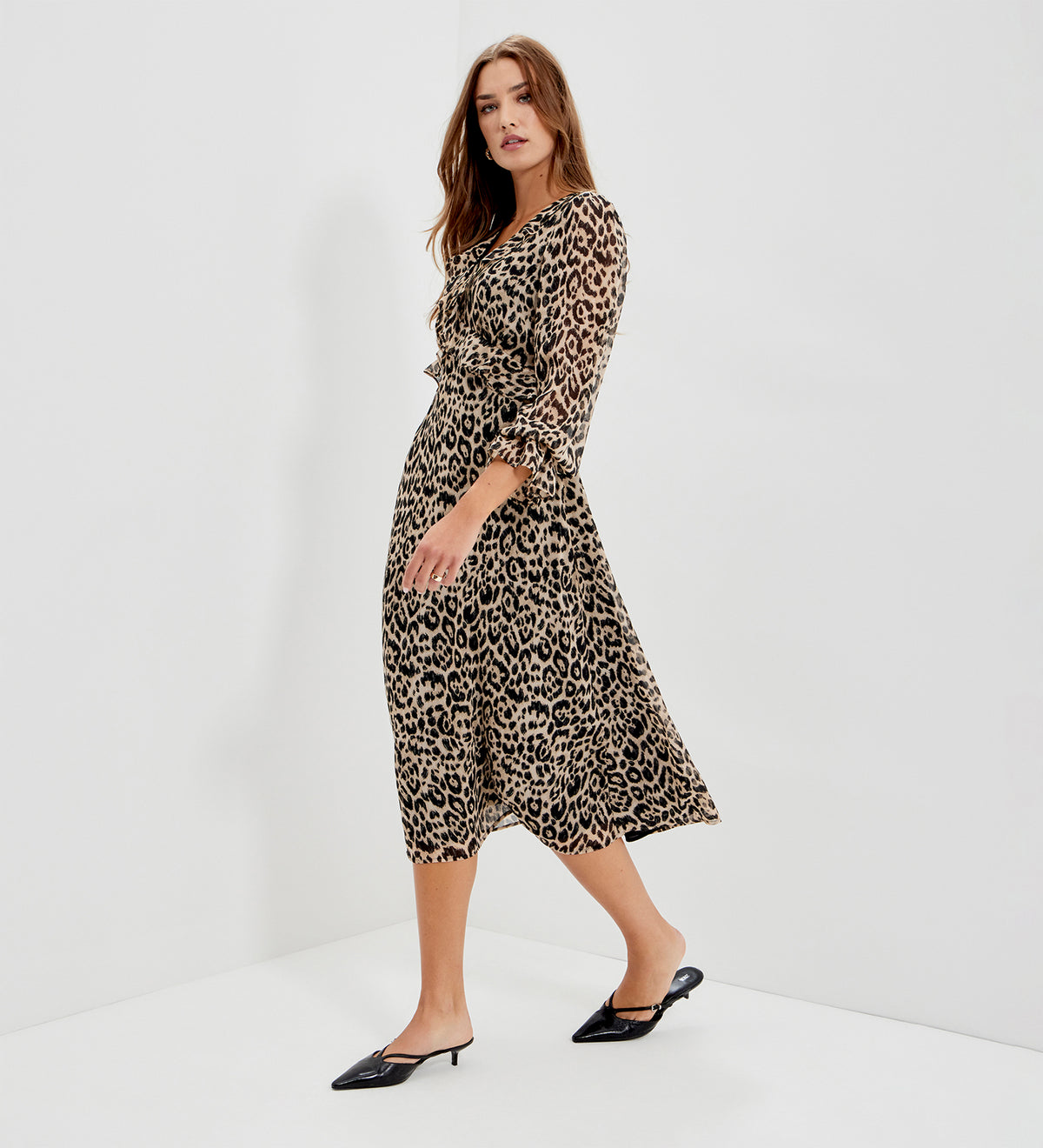 A woman modeling Veronica Natural Animal Ruffle Empire Waist Midi Dress, paired with black pointed-toe mule heels, set against a clean white studio background.