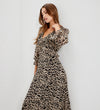 A woman wearing Veronica Natural Animal Ruffle Empire Waist Midi Dress, standing against a plain light gray wall.