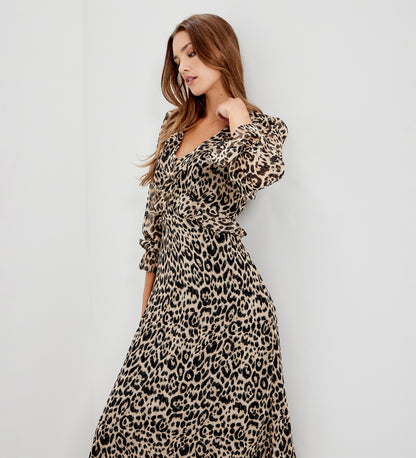 A woman wearing Veronica Natural Animal Ruffle Empire Waist Midi Dress, standing against a plain light gray wall.