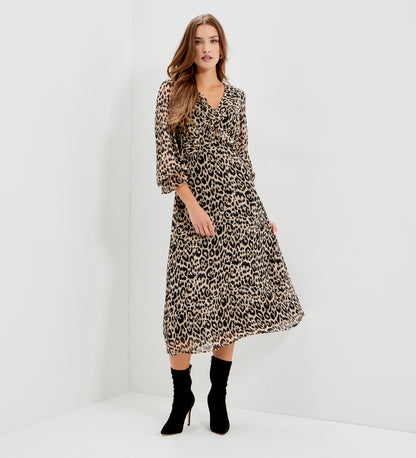 A woman modeling Veronica Natural Animal Ruffle Empire Waist Midi Dress, paired with black ankle boots, standing in a white studio corner.