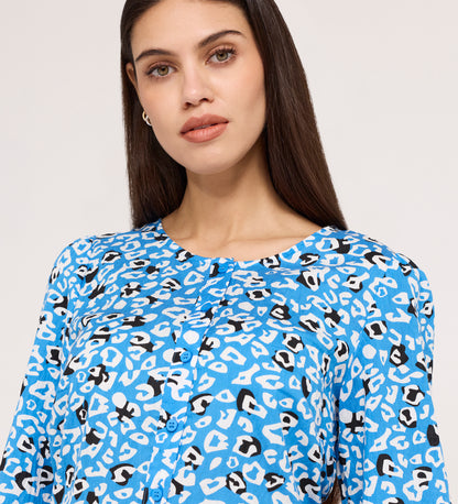 A woman with long brown hair wears the Bel Blue Leopard Cotton Blouse, a blue long-sleeve button-up featuring a white and black abstract animal print, while facing the camera against a plain light background.