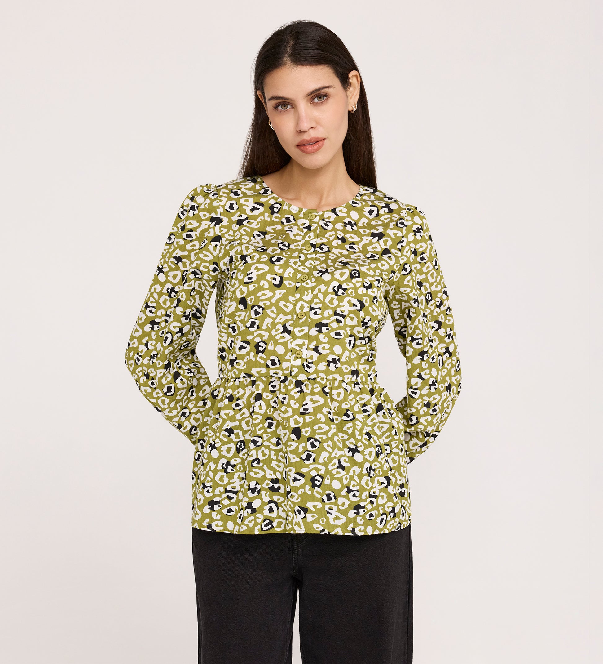 A woman with long dark hair wears the Bel Green Leopard Cotton Blouse, featuring blouson sleeves and a yellow-green leopard print, paired with black pants against a plain light background.