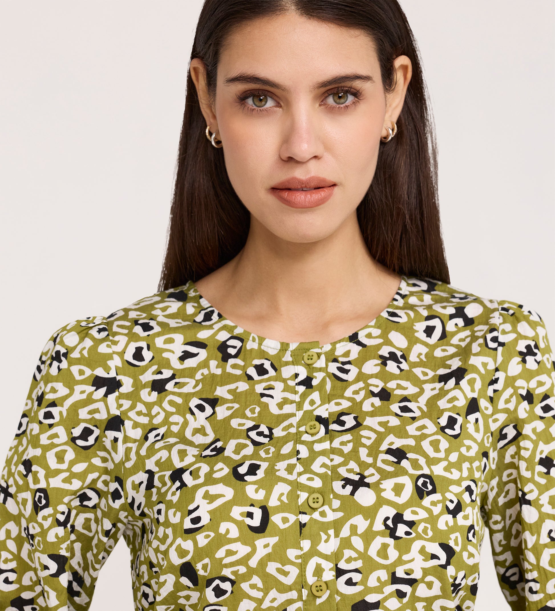 A woman with straight dark hair, gold hoop earrings, and the Bel Green Leopard Cotton Blouse—featuring a white and black abstract leopard print—poses against a plain light background.