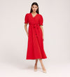 A woman stands against a plain background wearing the Everleigh Red Crepe Midi Dress, featuring a bright red hue, faux wrap neckline, puffed sleeves, waist tie, and nude pointed-toe heels.