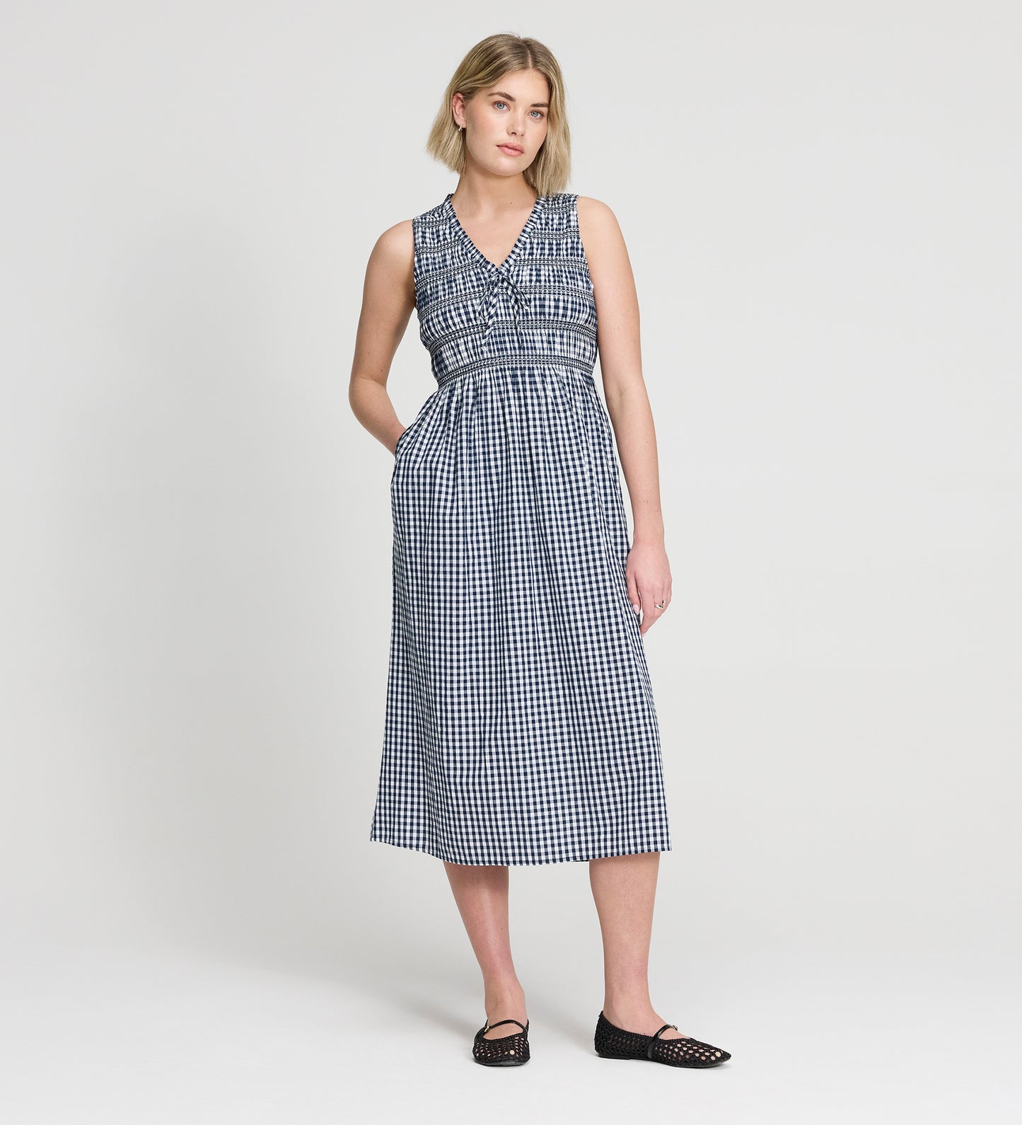 Woman wearing Hadlee Navy Cotton Gingham Shirred Bodice Sleeveless Midi Dress on a white background