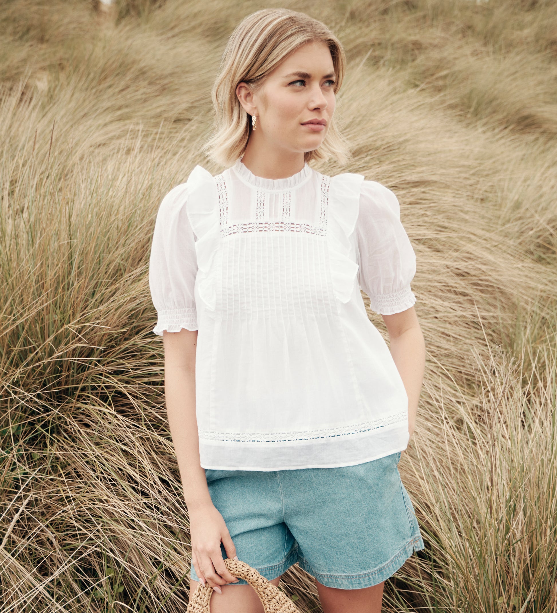 Woman wearing Jolin White Lace Cotton Puff Sleeve Top and denim shorts standing in tall grass.