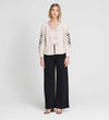 Woman wearing Karlee Neutral Stripe Embroidered Cotton Tie Front Blouse and black pants on a white background