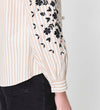 Close-up of a person wearing Karlee Neutral Stripe Embroidered Cotton Tie Front Blouse on a plain background