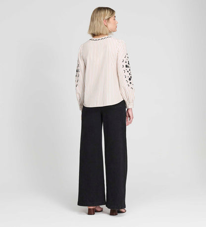 Woman wearing a Karlee Neutral Stripe Embroidered Cotton Tie Front Blouse and black pants on a white background