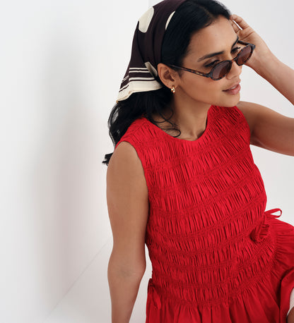 Woman wearing Malani Red Cotton Poplin Shirred Peplum Shell Top and sunglasses with a headscarf on a white background