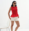 Woman wearing a Malani Red Cotton Poplin Shirred Peplum Shell Top and white shorts on a white background