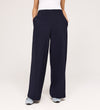 Wearing the Nat Navy Gaberdine Twill Wide Leg Trousers, a person with hands in pockets, white top, and gray sneakers stands against a plain light background.