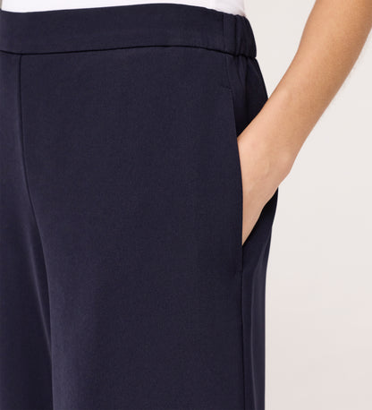 A person wearing Nat Navy Gaberdine Twill Wide Leg Trousers with their right hand in the pocket, shown waist down against a light background.