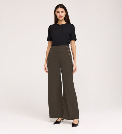 A woman poses against a plain background wearing a black short-sleeve top, black heels, and Nellie Mushroom Gaberdine Twill Wide Leg Trousers with decorative side buttons.