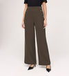 Wearing the Nellie Mushroom Gaberdine Twill Wide Leg Trousers with decorative side buttons, a black short-sleeve top, and black pointed-toe heels, a person stands against a plain background.
