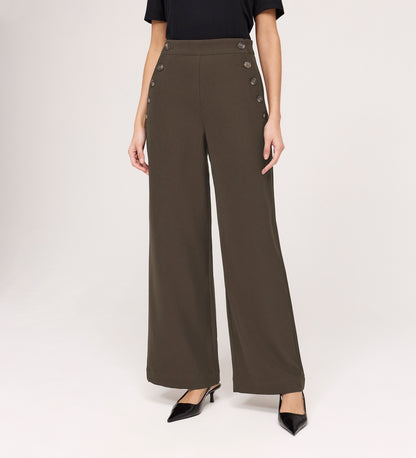 Wearing the Nellie Mushroom Gaberdine Twill Wide Leg Trousers with decorative side buttons, a black short-sleeve top, and black pointed-toe heels, a person stands against a plain background.