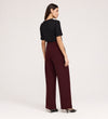 A woman, seen from behind, wears a black short-sleeve top, black heels, and Nellie Burgundy Gaberdine Twill Wide Leg Trousers against a plain light background.