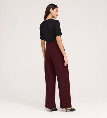 A woman, seen from behind, wears a black short-sleeve top, black heels, and Nellie Burgundy Gaberdine Twill Wide Leg Trousers against a plain light background.