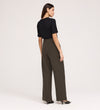 A woman stands facing away, wearing a black short-sleeve top, black low-heeled shoes, and Nellie Mushroom Gaberdine Twill Wide Leg Trousers against a plain light background.
