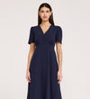 A woman wears the Nieve Navy Crepe Midi Dress, featuring short sleeves, a V-neckline, empire waist, and bodice buttons. She stands against a plain light background, facing forward with a neutral expression.
