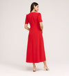 A woman faces away, wearing the Nieve Red Crepe Midi Dress with a square neckline and empire waist. The short-sleeved, midi dress pairs elegantly with beige heeled sandals against a plain light background.