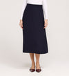A woman, her face not visible, stands against a light background wearing the Ramona Navy Rich Crepe Midi Skirt paired with a fitted white long-sleeve top and pointed maroon flats.