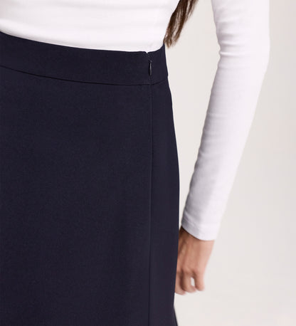 A person is shown from the back and waist down wearing a white long-sleeve shirt and the Ramona Navy Rich Crepe Midi Skirt, with one arm relaxed by their side.